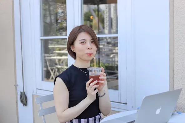 パソコンの前で飲み物を手にする川端アスミさん